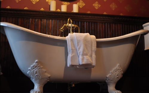 A vintage clawfoot bathtub with a white towel draped over the side, set against a decorative wall.