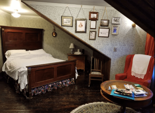 Cozy bedroom with a sloped ceiling, featuring a bed, chair, side table, and framed pictures on the wall.