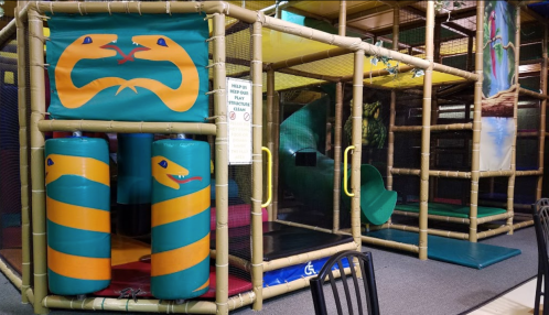 Colorful indoor play structure featuring snake designs, slides, and climbing areas, surrounded by safety netting.