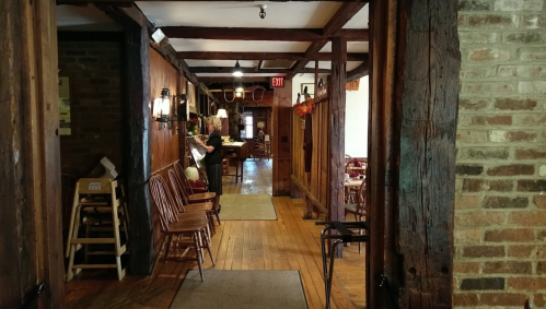 A rustic hallway with wooden beams, chairs, and a bar area, creating a warm, inviting atmosphere.