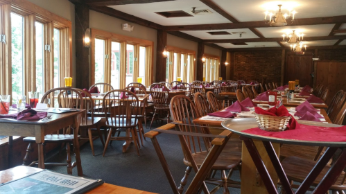Cozy restaurant interior with wooden tables, chairs, and large windows, set for dining with purple napkins and drinks.