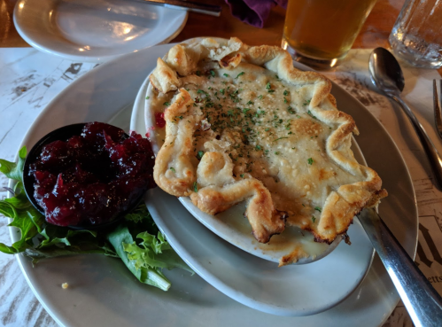 A baked dish with a golden crust, served with a side of cranberry sauce and a small salad on a white plate.