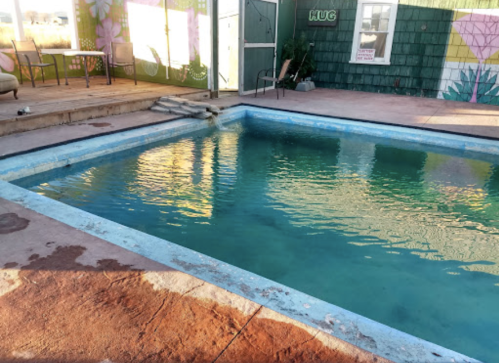 A partially filled swimming pool with clear water, surrounded by a patio and colorful mural-covered walls.
