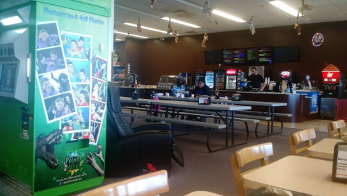A spacious indoor area with tables, a snack bar, and a colorful photo booth featuring dinosaur graphics.