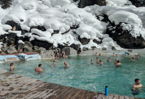 People enjoying a hot spring surrounded by snow-covered rocks and a winter landscape.