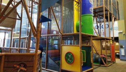 Indoor play structure with colorful tubes, climbing areas, and soft play equipment in a spacious environment.