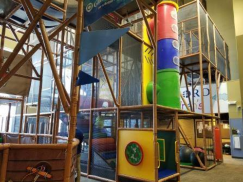 Indoor play structure featuring colorful tubes, climbing areas, and various play panels for children.
