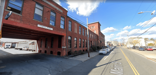 A red brick building with large windows, a loading area, and parked cars along Main Street under a blue sky.