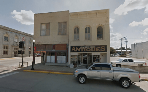 A two-story building with a sign reading "Juanita's House Antiques" and parked cars on the street.