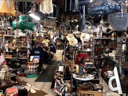 A cluttered antique shop filled with various vintage items, bicycles, and eclectic decor hanging from the ceiling.