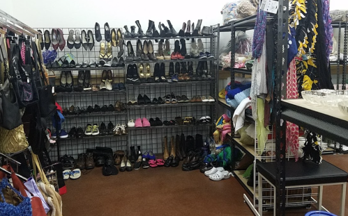 A cluttered thrift store display featuring various shoes and clothing items on racks and shelves.