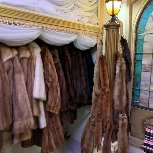 A display of various fur coats hanging on a rack, with a stained glass door in the background.