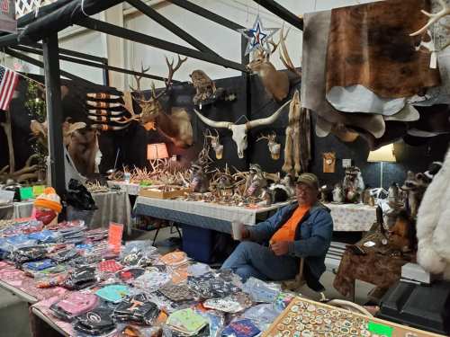 A vendor sits at a booth filled with merchandise, surrounded by mounted animal heads and various crafts.