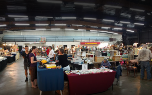 A bustling indoor market with vendors, shoppers, and various stalls displaying goods in a large, well-lit space.