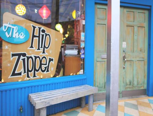 A colorful storefront with a sign reading "The Hip Zipper" and a wooden bench in front of a blue wall.