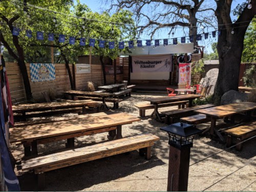 Outdoor seating area with wooden tables, festive decorations, and trees in a casual, inviting atmosphere.