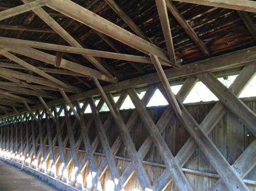 Interior view of a covered bridge, showcasing wooden beams and a crisscross pattern along the walls.