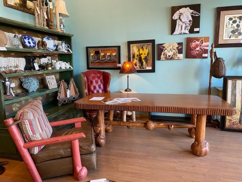A cozy room featuring a wooden table, a red chair, and a display shelf with various decorative items and artwork.