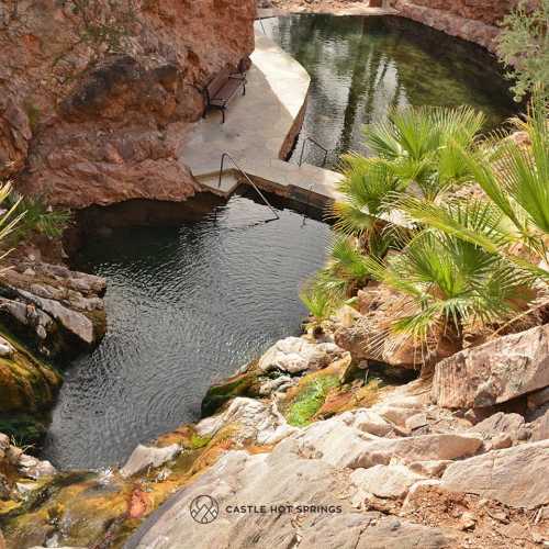 A serene natural pool surrounded by rocky terrain and lush greenery, with a bench nearby for relaxation.