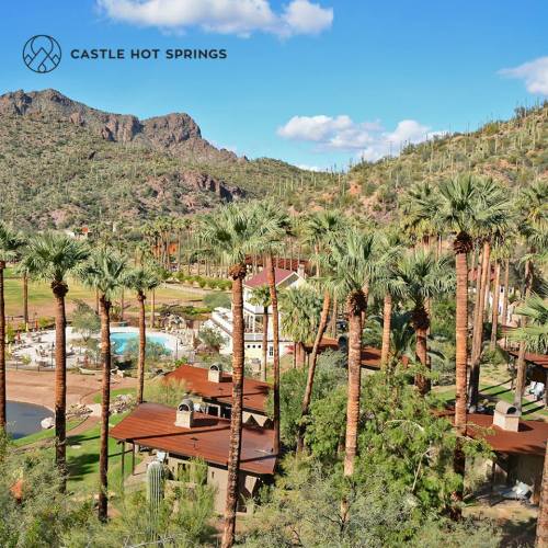 A scenic view of Castle Hot Springs, featuring palm trees, mountains, and a clear blue sky.