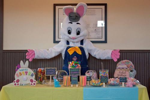 A costumed bunny stands behind a colorful candy display with various treats for Easter celebrations.