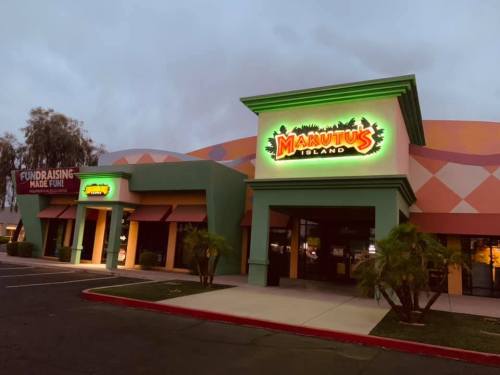 Exterior of Makutu's Island, a colorful building with neon signage, surrounded by palm trees at dusk.