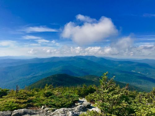 A panoramic view of lush green mountains under a blue sky with scattered clouds.