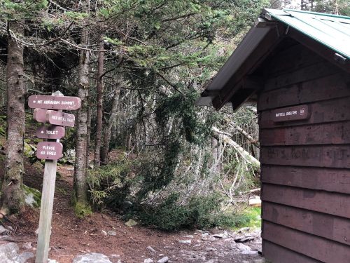 A wooden signpost with trail directions next to a rustic cabin in a forested area.