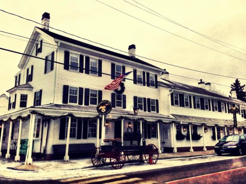 A historic white building with black shutters, an American flag, and a horse-drawn carriage in front, set in winter.