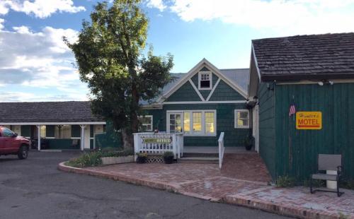 A green motel building with a porch, surrounded by trees and a red truck parked nearby under a blue sky.