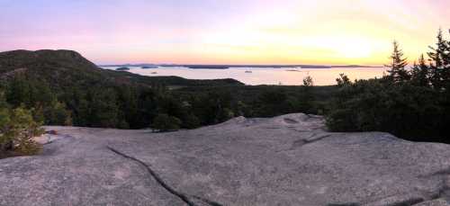 Panoramic view of a serene landscape at sunset, featuring water, islands, and trees against a colorful sky.