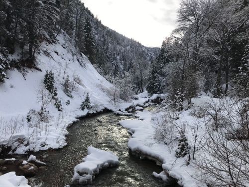 A serene winter landscape featuring a snow-covered river winding through a forested valley.