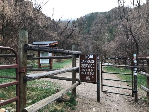 A wooden gate at a trailhead with a sign stating "No Garbage Service: Pack It In, Pack It Out" surrounded by trees.