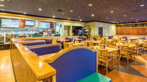 Interior of a restaurant featuring empty tables, colorful seating, and a counter with a display of food options.