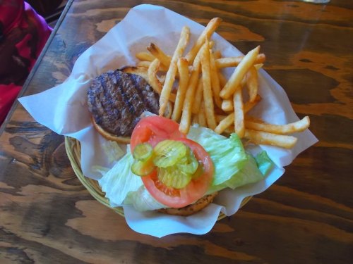 A basket containing a hamburger patty on a bun, topped with lettuce, tomato, pickles, and a side of French fries.