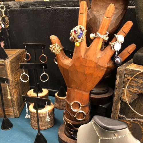 A wooden hand display showcasing various rings and earrings, with jewelry arranged on stands and a bust.