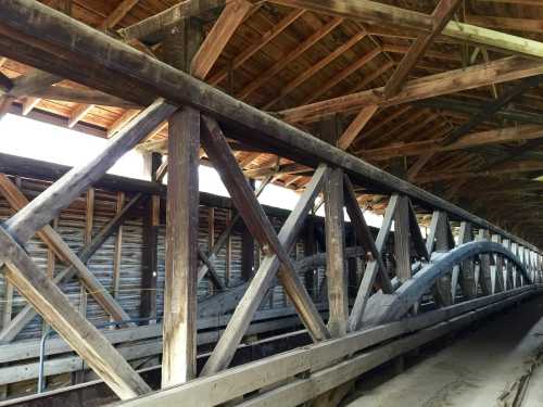 Interior view of a wooden covered bridge, showcasing intricate wooden beams and a rustic, open structure.