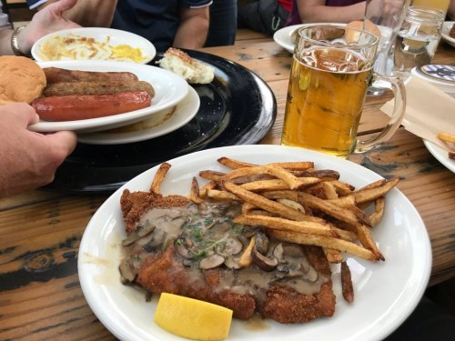 A plate of fried chicken with gravy, fries, and a lemon wedge, alongside a mug of beer and other dishes in the background.