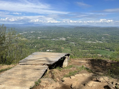 A wooden overlook platform with a scenic view of rolling hills and valleys under a blue sky with scattered clouds.