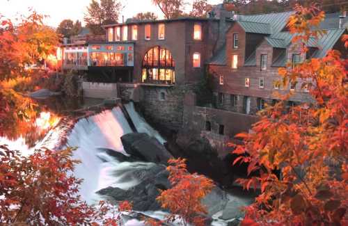 A scenic view of a waterfall beside a historic building, surrounded by vibrant autumn foliage.