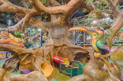 Colorful indoor play area featuring a large tree structure with animal sculptures and slides.