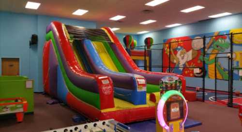 Colorful indoor bounce house slide in a play area with vibrant murals and various play equipment.