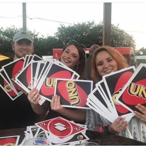 A group of three friends holding large UNO cards, smiling and enjoying a sunny outdoor setting.