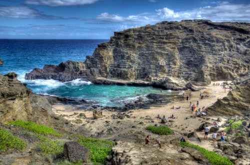 A scenic beach with rocky cliffs, turquoise water, and people enjoying the sun on the sandy shore.