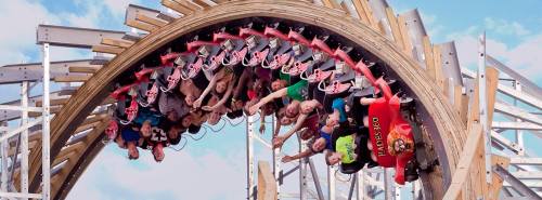 A roller coaster with riders upside down, enjoying the thrill of the ride against a blue sky backdrop.