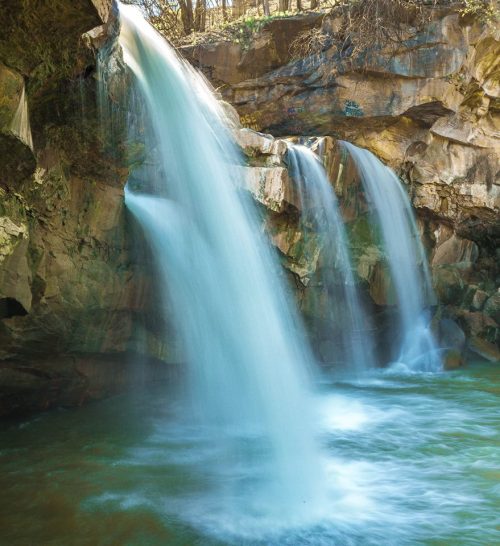 A serene waterfall cascading over rocky cliffs into a tranquil pool below, surrounded by lush greenery.