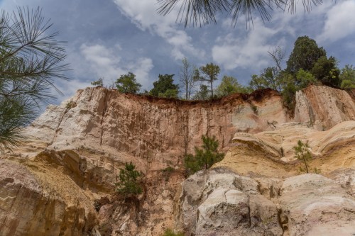 A rocky cliff with layered colors and sparse trees under a cloudy sky.