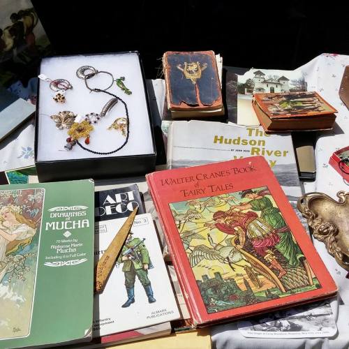 A collection of vintage books, jewelry, and art displayed on a table in bright sunlight.