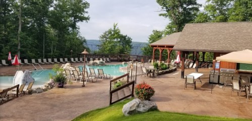 A serene pool area surrounded by trees, featuring lounge chairs, a gazebo, and colorful flowers.