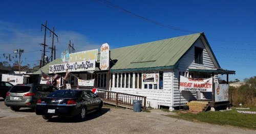 A small, white building with a green roof, featuring signs for a seafood market and a meat market, surrounded by parked cars.